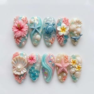 May include: A set of ten press-on nails featuring a tropical ocean theme. The designs include 3D elements such as pink hibiscus flowers, white plumeria, blue sea turtles, starfish, seashells, coral, and small pearls on pastel blue and cream bases.