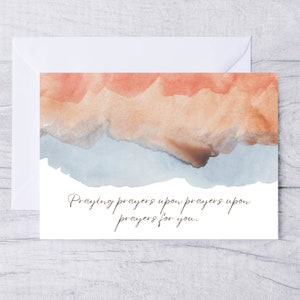 May include: A watercolor card with a light blue, brown, and orange abstract design. The card has the text "Praying prayers upon prayers for you."