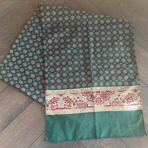 Peut inclure: Une écharpe rectangulaire présentant une base vert foncé avec un motif répétitif de petits cercles rouges et blancs. Le bord inférieur affiche une large bordure ornée dans des tons de rouge, d'or et de blanc avec des motifs cachemire complexes.