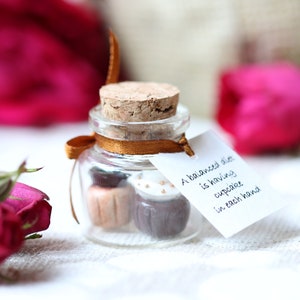 May include: A small glass jar with a cork lid contains two miniature cupcakes, one chocolate and one vanilla. A white tag attached to the jar reads "A balanced diet is having cupcakes in each hand."