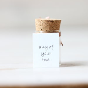 May include: A small glass bottle with a cork stopper and a white label. The label has the text "any of your text" written on it.