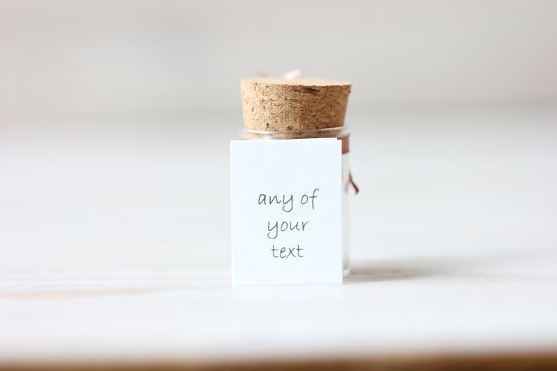 May include: A small glass bottle with a cork stopper and a white label. The label has the text "any of your text" written on it.