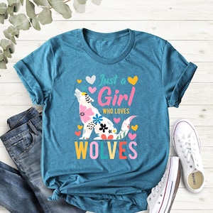 May include: A teal blue t-shirt with a colorful wolf graphic and the text "Just a Girl Who Loves Wolves".