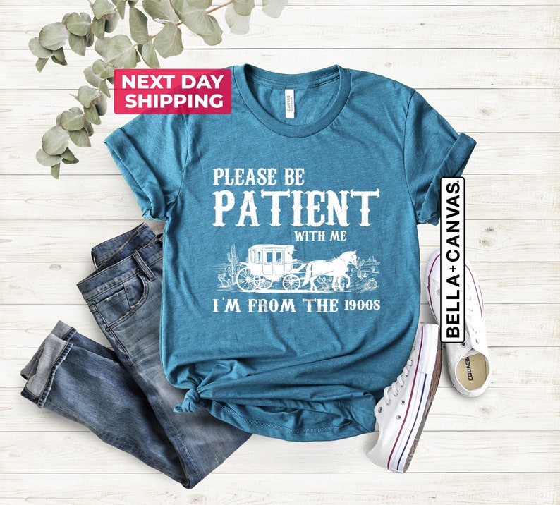 May include: Teal blue t-shirt with white text that reads "Please be patient with me I'm from the 1900s". The text is accompanied by a graphic of a horse-drawn carriage.