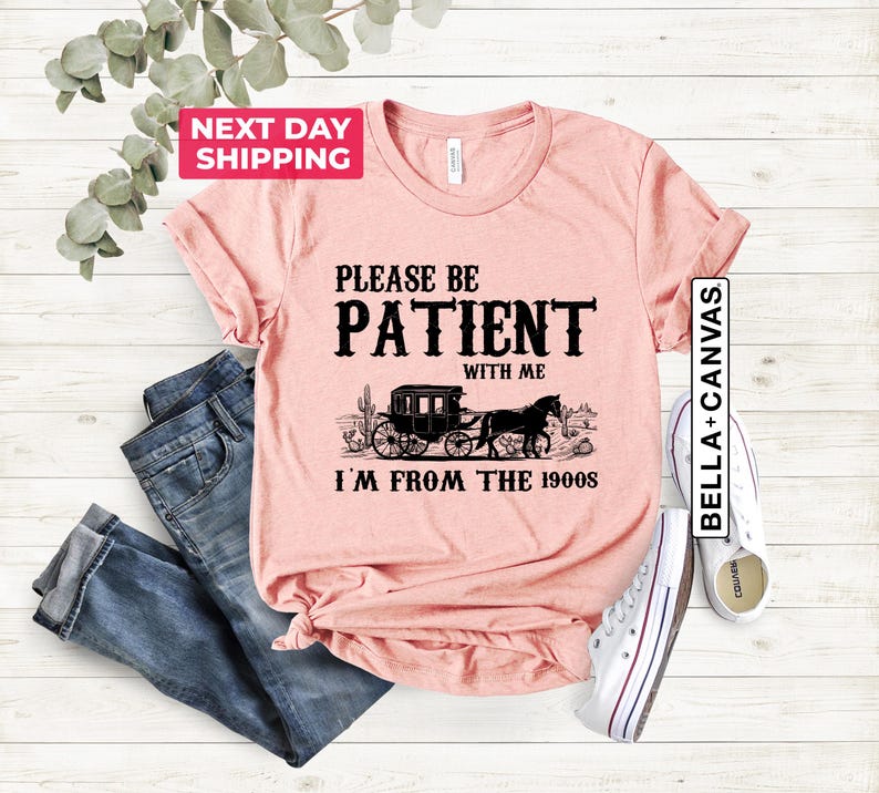May include: A pink t-shirt with a black graphic that says "Please be patient with me I'm from the 1900s". The graphic also includes a black and white illustration of a horse-drawn carriage.