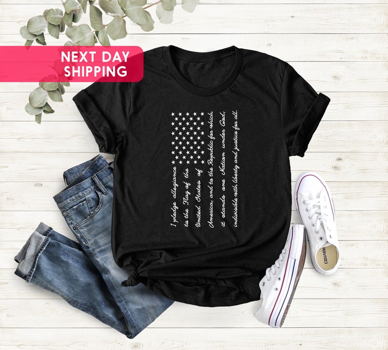 K&ouml;nnte beinhalten: Schwarzes T-Shirt mit einem wei&szlig;en amerikanischen Flaggen-Motiv und dem Text "Ich schw&ouml;re Treue zur Flagge der Vereinigten Staaten von Amerika und der Republik, f&uuml;r die sie steht, eine Nation unter Gott, unteilbar mit Freiheit und Gerechtigkeit f&uuml;r alle."