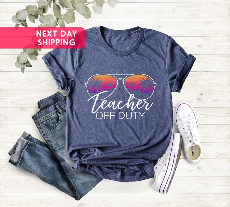 May include: A navy blue t-shirt with a white graphic of sunglasses reflecting palm trees and a sunset. The text "Teacher Off Duty" is printed below the sunglasses.