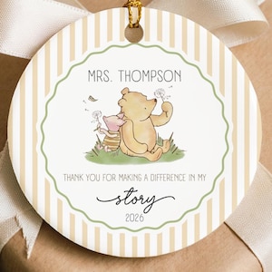 Puede incluir: Un adorno redondo de cerámica con un fondo de rayas verticales beige y blancas. El centro muestra una ilustración de Winnie the Pooh y Piglet con el texto "MRS. THOMPSON", "THANK YOU FOR MAKING A DIFFERENCE IN MY story" y "2026".