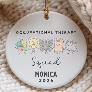 Puede incluir: Un adorno redondo de cerámica blanca con el texto OCCUPATIONAL THERAPY Squad MONICA 2026. El diseño incluye ilustraciones coloridas de una pieza de rompecabezas, bombilla, mariposa, toalla enrollada y cerebro, todos tomados de la mano.