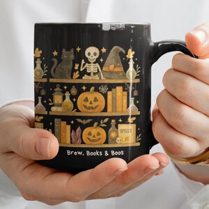 Puede incluir: Taza de cerámica negra con un diseño de Halloween. La taza presenta ilustraciones de un gato negro, un esqueleto, un sombrero de bruja, calabazas, libros y el texto "Brew, Books & Boos". La taza tiene una capacidad de 325 ml.