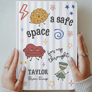 Puede incluir: Un cuaderno con una cubierta de rayas azul claro y blancas con el texto "a safe space for my thoughts" y "TAYLOR Brain Dump". La cubierta incluye ilustraciones de dibujos animados de un cerebro, un sofá, un reloj de arena, estrellas y flores.