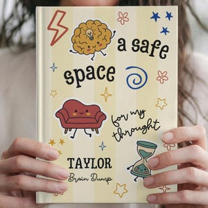 Puede incluir: Un diario de tapa dura con rayas de color amarillo claro y blanco que presenta el texto "a safe space for my thought" y "TAYLOR Brain Dump". Las ilustraciones incluyen un cerebro con una bombilla, un sofá rojo y un reloj de arena.