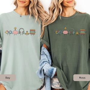 Comfort Colors Autism Doodle Characters Shirt featuring colorful, hand-drawn inclusive characters. Neatly styled next to classroom supplies, making it an ideal inclusion shirt, autism teacher shirt, and back to school shirt.