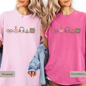 Comfort Colors Autism Doodle Characters Shirt featuring colorful, hand-drawn inclusive characters. Neatly styled next to classroom supplies, making it an ideal inclusion shirt, autism teacher shirt, and back to school shirt.