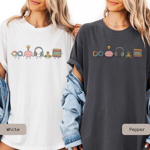 Comfort Colors Autism Doodle Characters Shirt featuring colorful, hand-drawn inclusive characters. Neatly styled next to classroom supplies, making it an ideal inclusion shirt, autism teacher shirt, and back to school shirt.