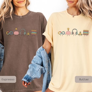 Comfort Colors Autism Doodle Characters Shirt featuring colorful, hand-drawn inclusive characters. Neatly styled next to classroom supplies, making it an ideal inclusion shirt, autism teacher shirt, and back to school shirt.