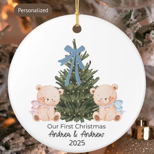 Puede incluir: Adorno navideño redondo de cerámica blanca con un diseño festivo. Presenta un árbol de Navidad verde con un lazo azul, dos osos de peluche y el texto "Our First Christmas Andrea & Andrew 2025".