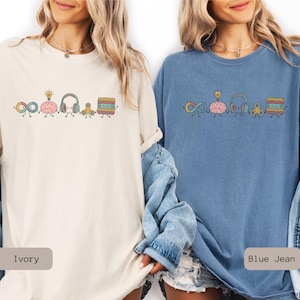 Comfort Colors Autism Doodle Characters Shirt featuring colorful, hand-drawn inclusive characters. Neatly styled next to classroom supplies, making it an ideal inclusion shirt, autism teacher shirt, and back to school shirt.
