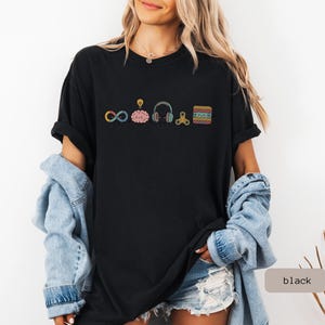 Comfort Colors Autism Doodle Characters Shirt featuring colorful, hand-drawn inclusive characters. Neatly styled next to classroom supplies, making it an ideal inclusion shirt, autism teacher shirt, and back to school shirt.