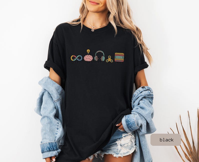 Comfort Colors Autism Doodle Characters Shirt featuring colorful, hand-drawn inclusive characters. Neatly styled next to classroom supplies, making it an ideal inclusion shirt, autism teacher shirt, and back to school shirt.