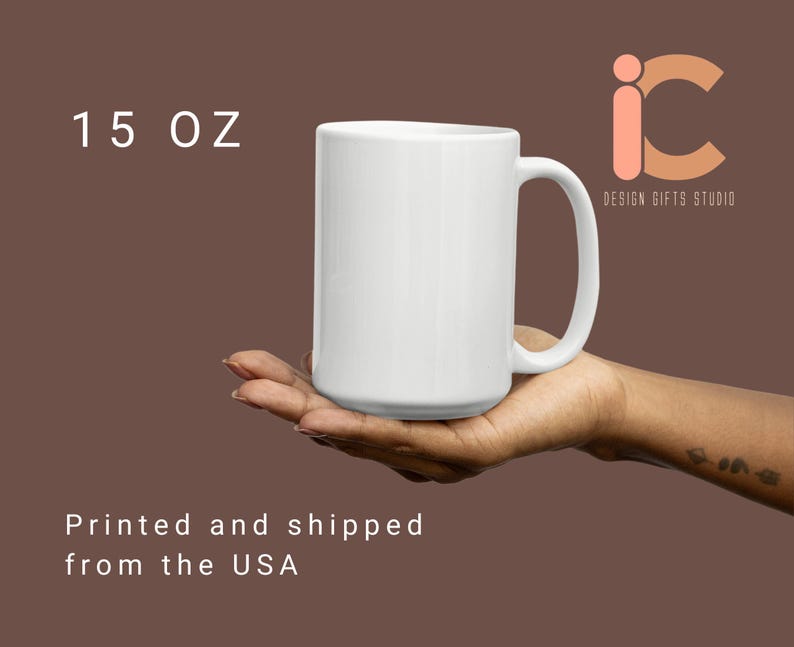May include: A white ceramic mug with a capacity of 15 oz. The mug has a large handle and is held in a person's hand. The mug is plain and has a glossy finish. The text "DESIGN GIFTS STUDIO" is visible.