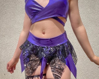 May include: A purple and black sequined crop top and skirt set. The top is a one-shoulder style with a cut-out detail. The skirt is a mini skirt with a ruffled hem.