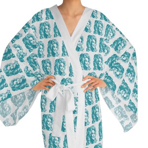 May include: A white robe with a teal pattern of a woman's face. The robe has a shawl collar, wide sleeves, and a white tie belt. The pattern is repeated across the robe's surface.