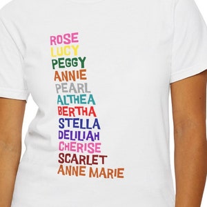 May include: White t-shirt with a vertical list of names printed in different colors: Rose, Lucy, Peggy, Annie, Pearl, Althea, Bertha, Stella, Delilah, Cherise, Scarlet, Anne Marie.