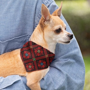 Può includere: Un piccolo cane marrone chiaro con una bandana fantasia è tenuto in una camicia di jeans blu. La bandana ha uno sfondo nero con disegni floreali rossi, blu e gialli. Il cane è un Chihuahua.