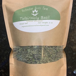 May include: A brown paper bag filled with dried Tulsi/Holy Basil leaves. The bag has a green and white label with the text "Restoration Acres Farm" and "Tulsi/Holy Basil". The label also includes the text "Dried leaf" and "Net Weight: 2 oz".