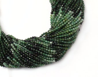 May include: Strands of faceted emerald green beads, varying in shades from light to dark, are displayed against a white background. The beads are strung together, forming a cascading effect. A green tassel is at the top. The Gems Valley logo is in the upper right corner.