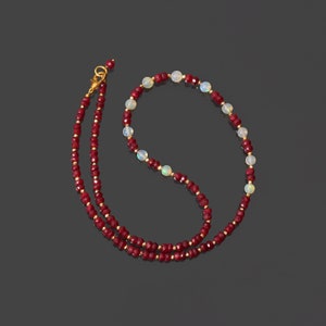 Puede incluir: Un collar de cuentas rojas y blancas con un cierre dorado. El collar está hecho de cuentas pequeñas y redondas y presenta un patrón repetitivo de cuentas rojas y blancas.