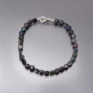 Può includere: Una collana di pietre preziose di opale nero con una chiusura in argento. La collana è composta da perline rotonde e piatte infilate su una catena d'argento.