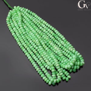 Könnte beinhalten: Eine Strähne grüner Edelsteinperlen, wahrscheinlich grüner Opal, mit einer glatten, abgerundeten Form. Die Perlen sind auf einem dünnen Draht aufgefädelt und in einem lockeren, fließenden Muster angeordnet.