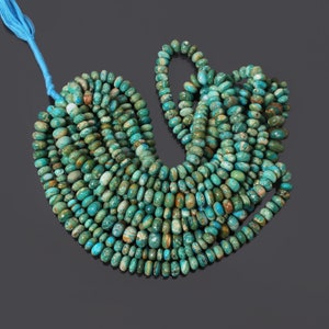 Op de afbeelding: Een streng turquoise blauwe edelsteen kralen, met een gevlekt patroon, in een ronde vorm. De kralen zijn geregen aan een koord en zijn gerangschikt in een cirkelvormig patroon.