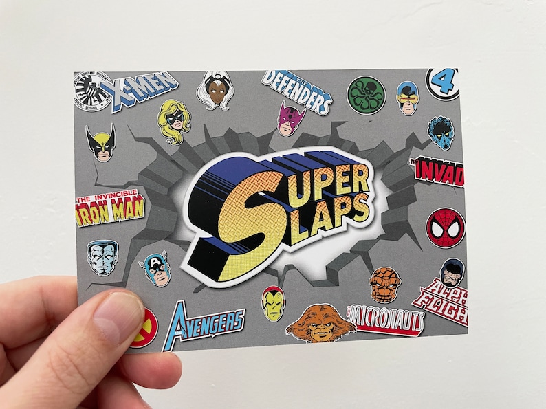 Colourful A6 sized postcard being held in left hand against a white background. Super Slaps branded with lots of Marvel super hero face and logo stickers.