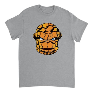 May include: A gray t-shirt with a graphic of The Thing's face from the Fantastic Four. The Thing's face is orange and brown with blue eyes.