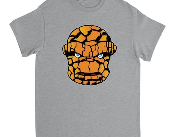 Op de afbeelding: Een grijs T-shirt met een afbeelding van het gezicht van The Thing uit de Fantastic Four. Het gezicht van The Thing is oranje en bruin met blauwe ogen.
