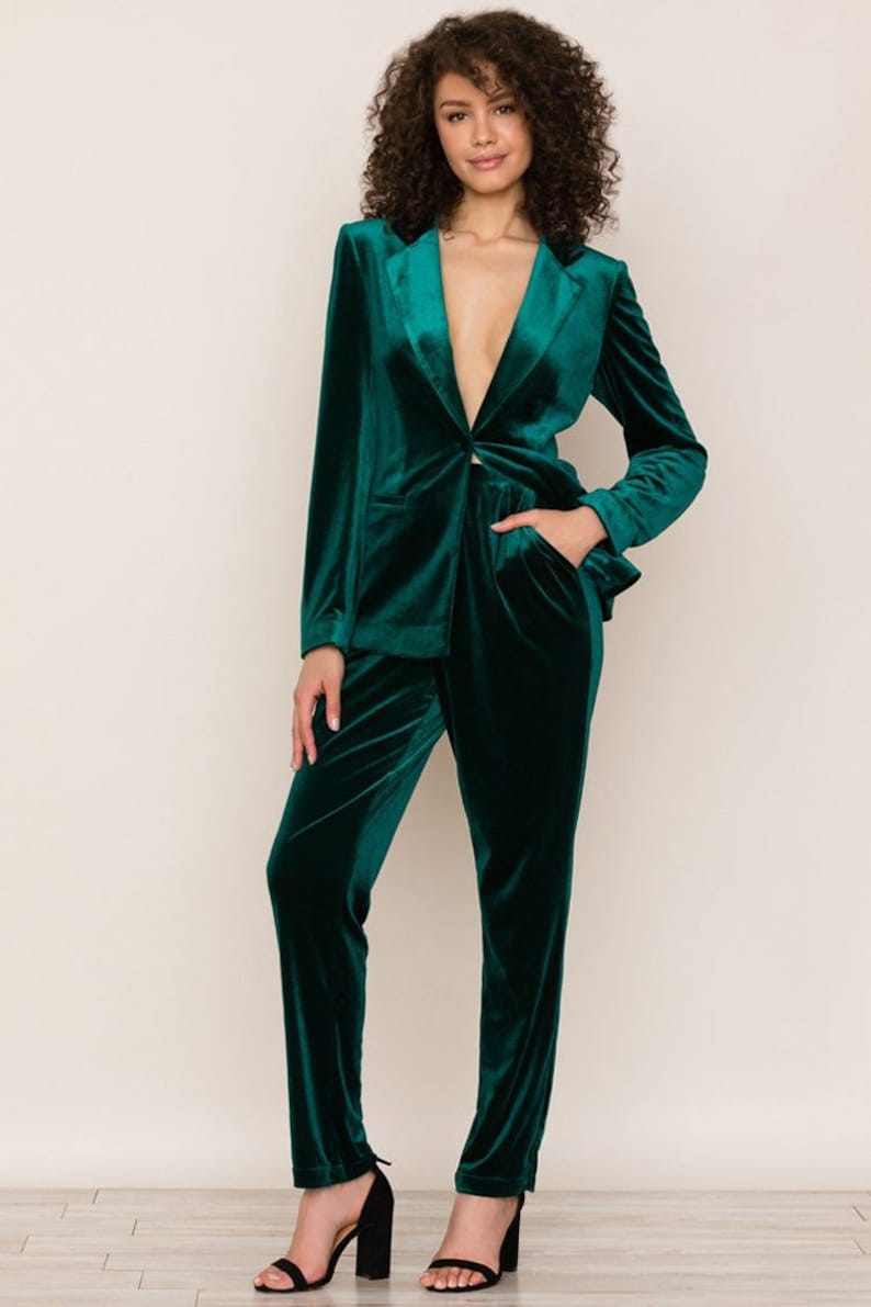 May include: A dark green velvet blazer and matching pants. The blazer has a single button closure and a deep V-neckline. The pants have a straight leg and a slightly cropped length.
