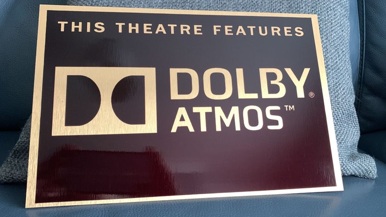 May include: A gold plaque with a black background that reads "This theatre features Dolby Atmos". The Dolby logo is a stylised "D" in a square.