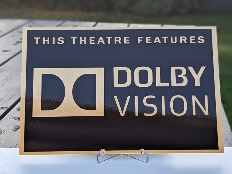 May include: A black plaque with gold lettering that reads "This theatre features Dolby Vision". The Dolby Vision logo is a stylised "D" with two curved lines.