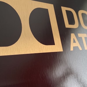 May include: A gold and black sign with the text "Dolby Atmos" in gold lettering.