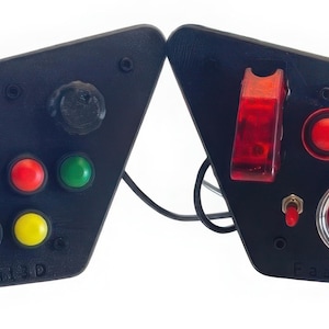 Könnte beinhalten: Zwei schwarze Bedienfelder mit verschiedenen Knöpfen und Schaltern. Ein Feld hat einen Knopf und mehrere farbige Knöpfe: blau, rot, grün, orange, schwarz und gelb. Das andere Feld hat einen roten Kippschalter, einen roten Knopf und einen großen roten "ENGINE START"-Knopf.