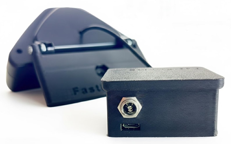 May include: Black electronic device with a rectangular box shape and a smaller, angled component behind it. The box has a port and a USB port. The angled component has the word "Fast" printed on it.