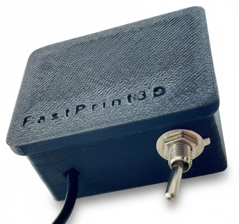 May include: A dark blue, rectangular 3D-printed device with the text "FastPrint3D" embossed on the top. It features a silver toggle switch on the side and a black cable extending from the bottom. The device has a textured surface.