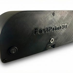 May include: Black 3D printer enclosure with the text "FastPrint3D" embossed on the side. The enclosure has a rounded top and features a power button, a USB port, and other ports. The device is designed to house a 3D printer.