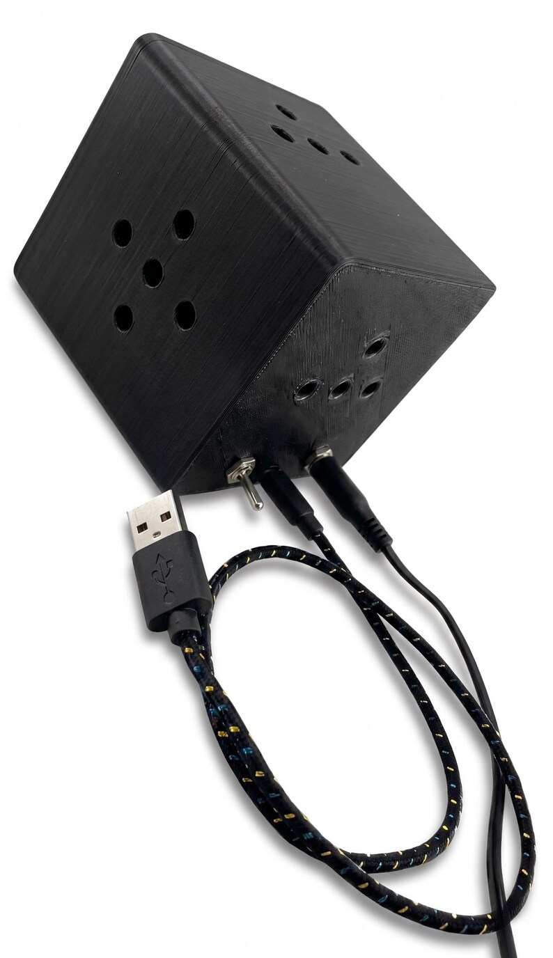 K&ouml;nnte beinhalten: Ein schwarzes, w&uuml;rfelf&ouml;rmiges elektronisches Ger&auml;t mit mehreren kreisf&ouml;rmigen &Ouml;ffnungen. Es verf&uuml;gt &uuml;ber einen Kippschalter, mehrere Eingangsanschl&uuml;sse und ein USB-Kabel mit einem gemusterten Kabel. Das Ger&auml;t scheint eine kundenspezifische elektronische Komponente oder ein Gadget zu sein.