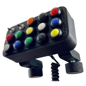 May include: Black control panel with an array of multi-colored buttons and toggle switches. The buttons are red, orange, yellow, green, blue, white, and black. The panel has a textured base and is designed for a simulator.