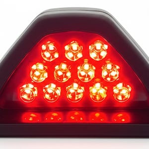 May include: A triangular red LED light with a dark frame. The light has 15 individual LED bulbs arranged in a triangular pattern. The lights are bright and appear to be illuminated.