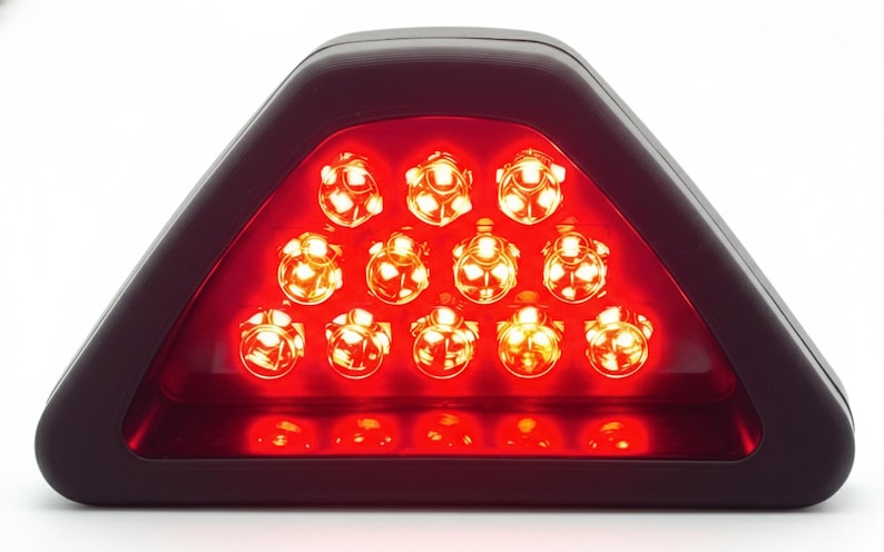 May include: A triangular red LED light with a dark frame. The light has 15 individual LED bulbs arranged in a triangular pattern. The lights are bright and appear to be illuminated.